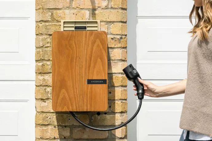 A woman is charging her electric car in front of a brick wall